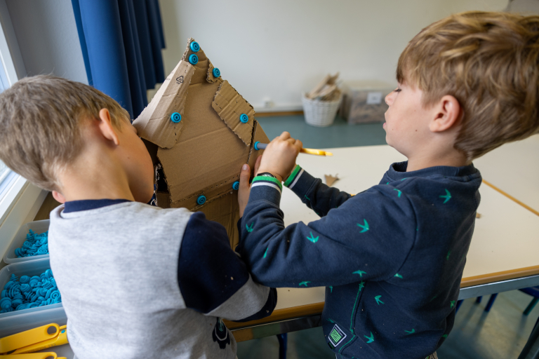 zwei Kinder bauen ein Haus aus Karton 